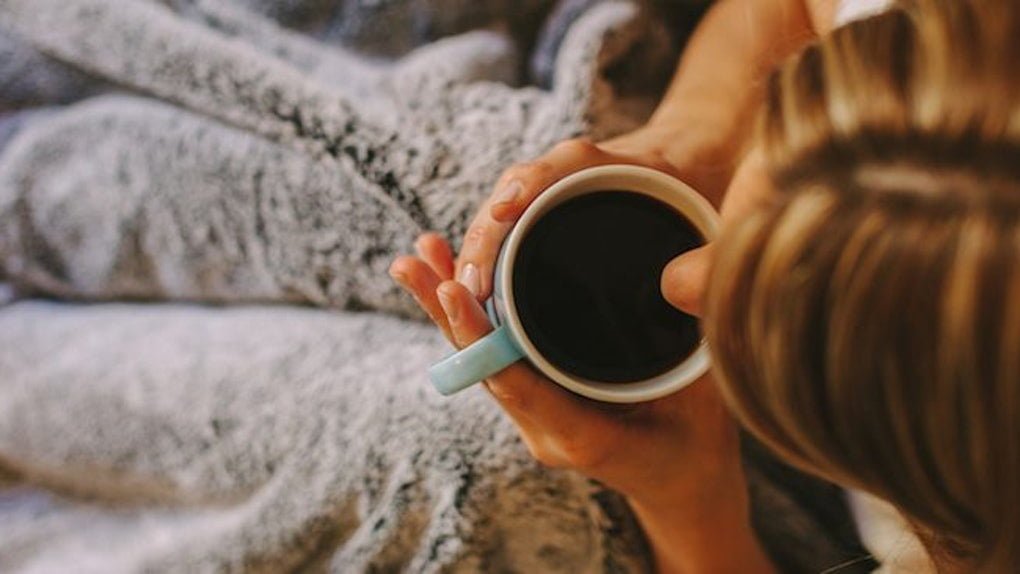 young woman drinking coffee in bed